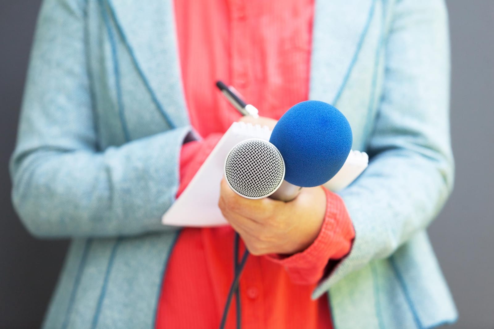 A reporter holding a microphone and notes while gathering a local story